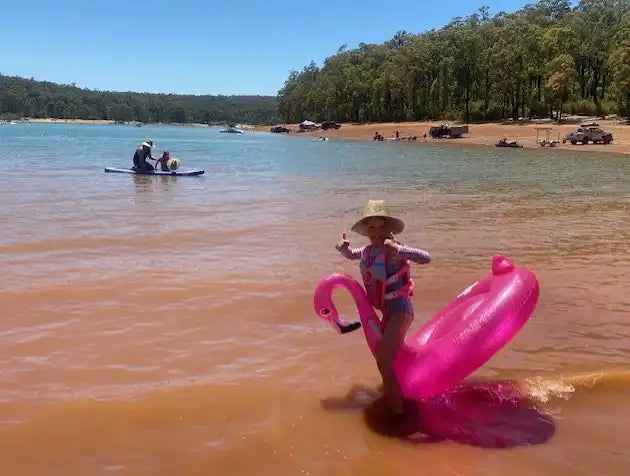 Child in a life vest on a pink flamingo inflatable float.