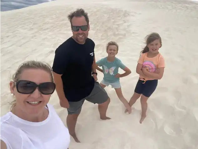 A family of four, including two adults and two children, standing on a sand dune.