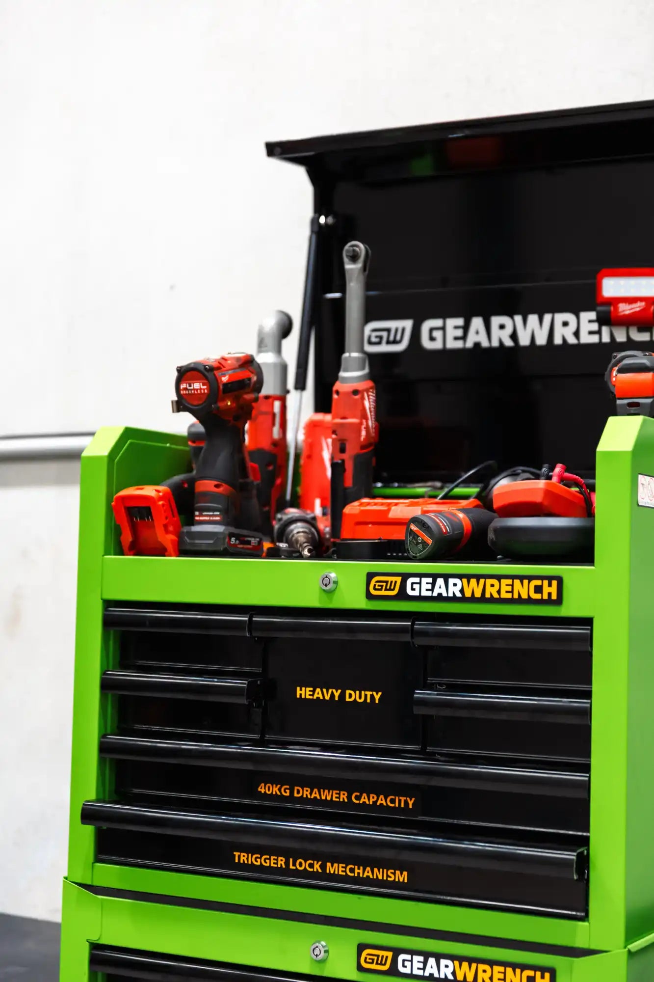 Green and black metal tool cabinet with multiple drawers and a top compartment filled with power tools.