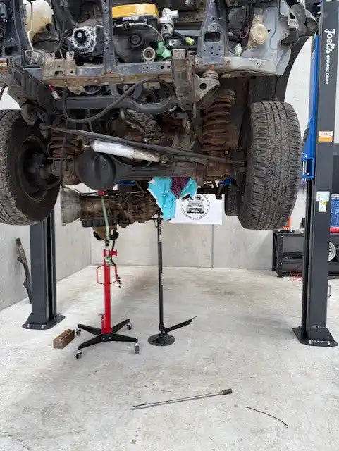 Underbody of a vehicle with a detached engine and transmission on a lift.