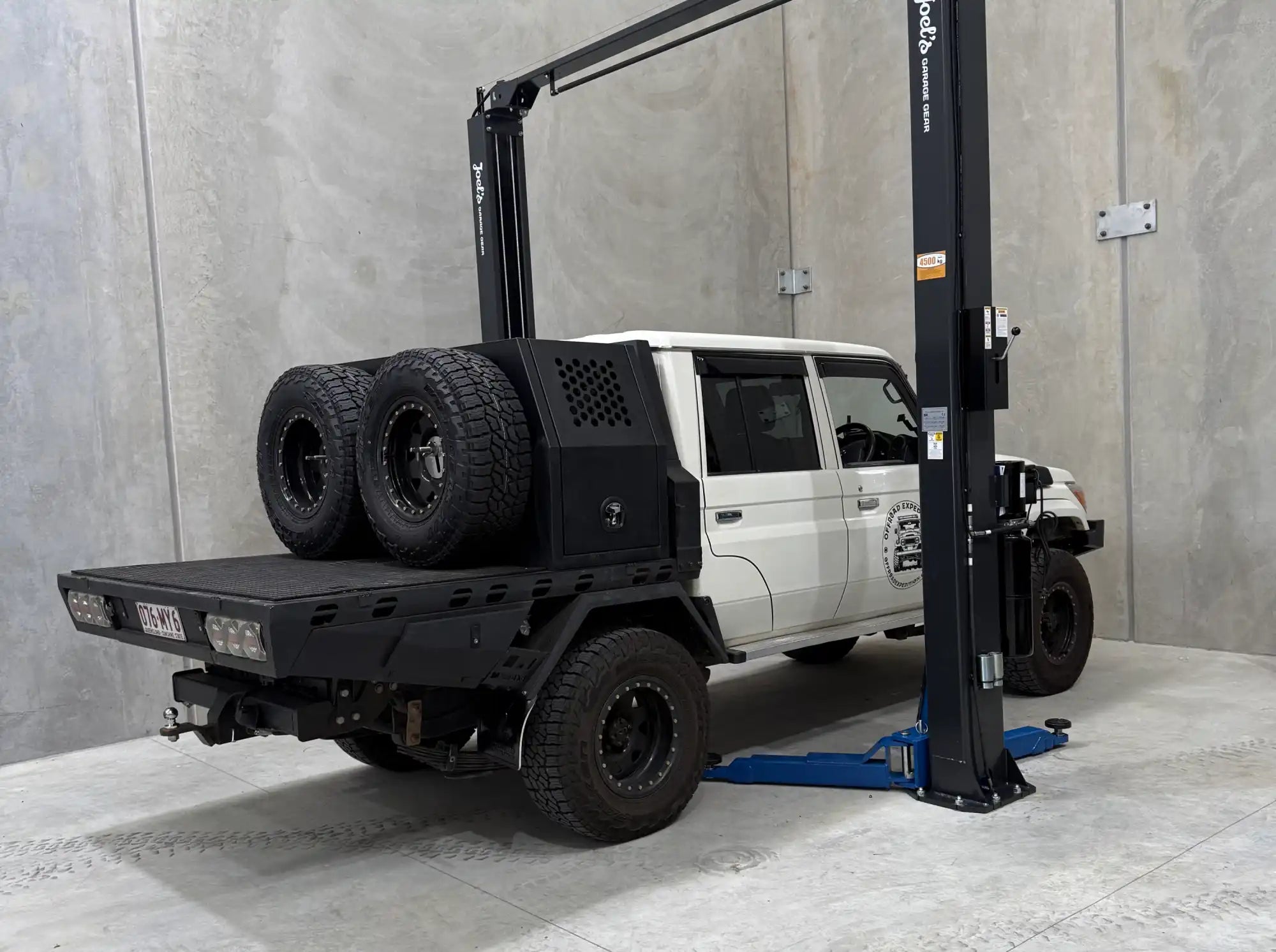White utility vehicle with a black flatbed tray and two spare tires.
